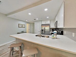 A modern kitchen with a large island, stainless steel appliances, and recessed ceiling lights. - Ciboney 1010 (Miramar Beach)