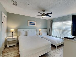 A hotel room with two beds, a ceiling fan, a framed picture on the wall, and a window with curtains. - Ciboney 1010 (Miramar Beach)