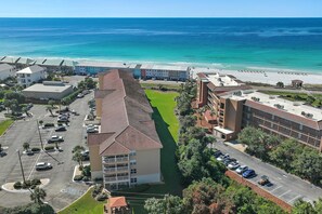 A hotel with a parking lot, a green lawn, and a view of the beach and ocean. - Ciboney 1010 (Miramar Beach)