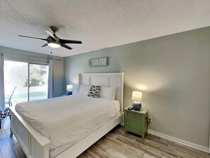 Une chambre à coucher comprenant un lit, une table de chevet, un ventilateur de plafond, une fenêtre et un panneau décoratif mural.
