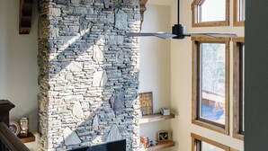 Habitación con vigas de madera a la vista, pared de piedra, televisor de pantalla plana y varias ventanas.