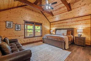 Un dormitorio tipo cabaña de madera con una cama, un sofá de cuero y un ventilador de techo.