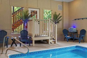 An indoor swimming pool with a wooden deck, chairs, and a table. - 8-Bedroom Smoky Mountain Cabin with Indoor Pool, Hot Tub & Game Room (Sevierville)