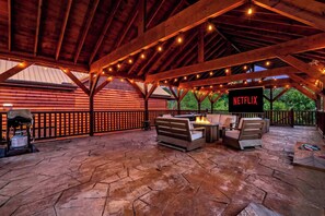 An outdoor patio with a stone floor, wooden furniture, a fire pit, and string lights. - A Happy Place | 8BR Cabin | Indoor Pool | GameRoom (Sevierville)