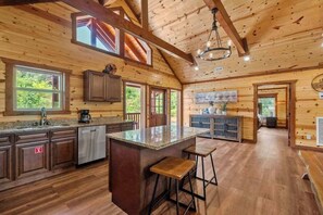 A spacious kitchen with wooden cabinets, a central island with stools, and a large window providing natural light. - A Happy Place | 8BR Cabin | Indoor Pool | GameRoom (Sevierville)