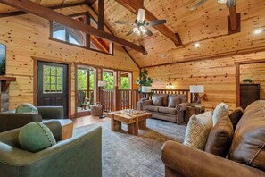 A log cabin interior with a high ceiling, wooden beams, a ceiling fan, a fireplace, and a cozy seating area with a couch and a coffee table. - 8-Bedroom Smoky Mountain Cabin with Indoor Pool, Hot Tub & Game Room (Sevierville)