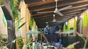 Uma área externa com assentos de madeira, ventilador de teto e vegetação.