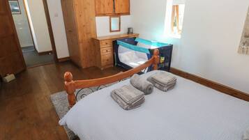 Um quarto com uma cama de madeira, um guarda-roupa de madeira, uma pequena escrivaninha e uma janela.
