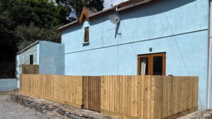 A building with a light blue exterior, a wooden fence, and a stone foundation. - Tor Cefn (Kidwelly)
