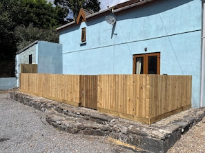 A building with a light blue exterior, a wooden fence, and a stone foundation. - Tor Cefn (Kidwelly)