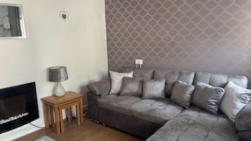 Uma sala de estar com sofá cinza, uma mesinha de madeira, lareira e papel de parede estampado.