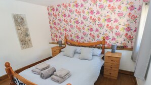 A neatly made bed with a floral-patterned headboard, a bedside table with a lamp, and a wooden nightstand. - Tor Cefn (Kidwelly)