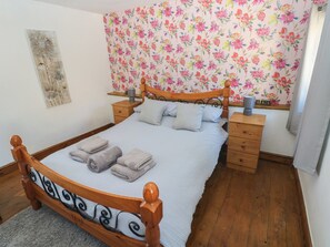 A neatly made bed with a floral-patterned headboard, a bedside table with a lamp, and a wooden nightstand. - Tor Cefn (Kidwelly)