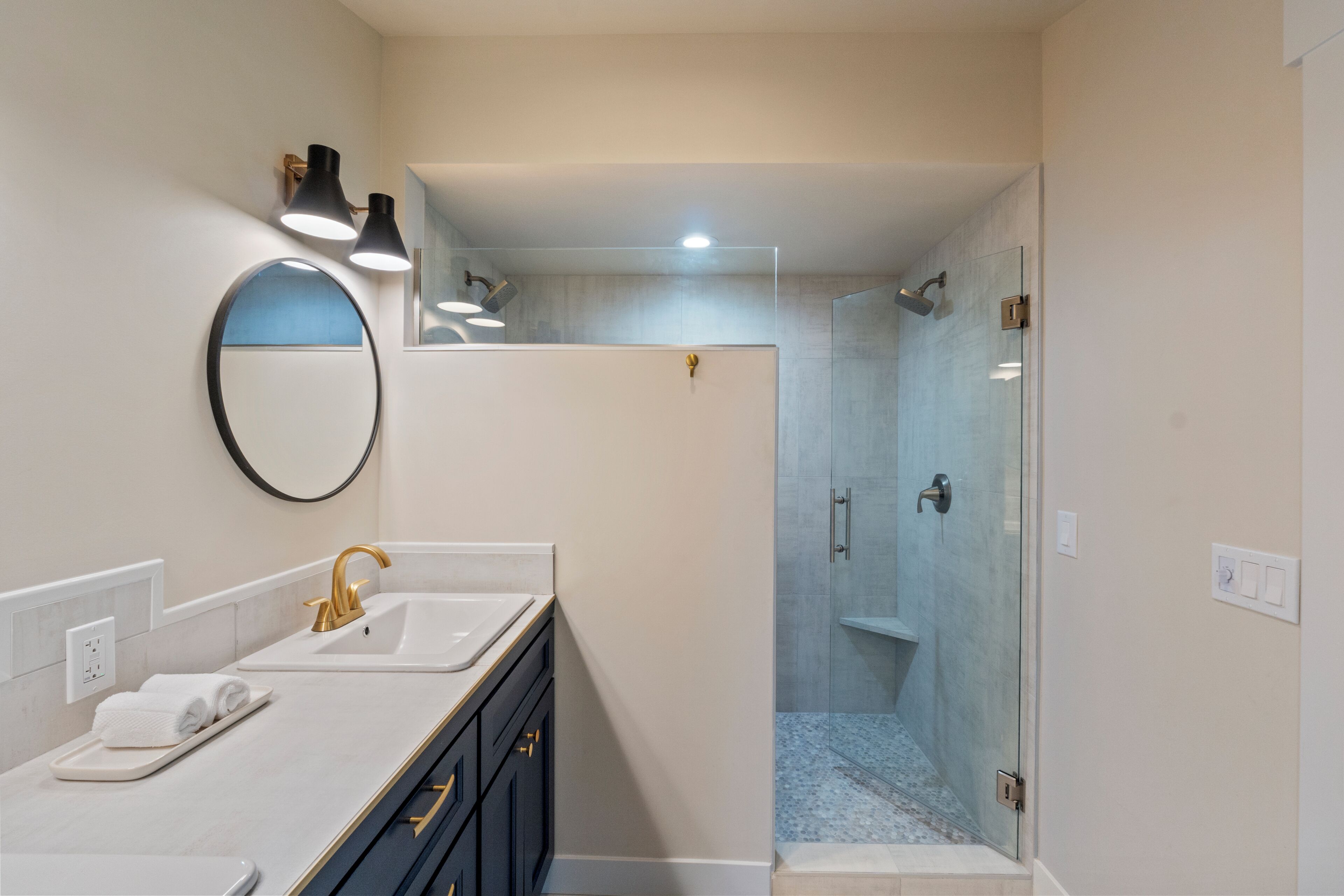 A modern bathroom with a dual sink vanity, a large mirror, and a glass-enclosed shower area.