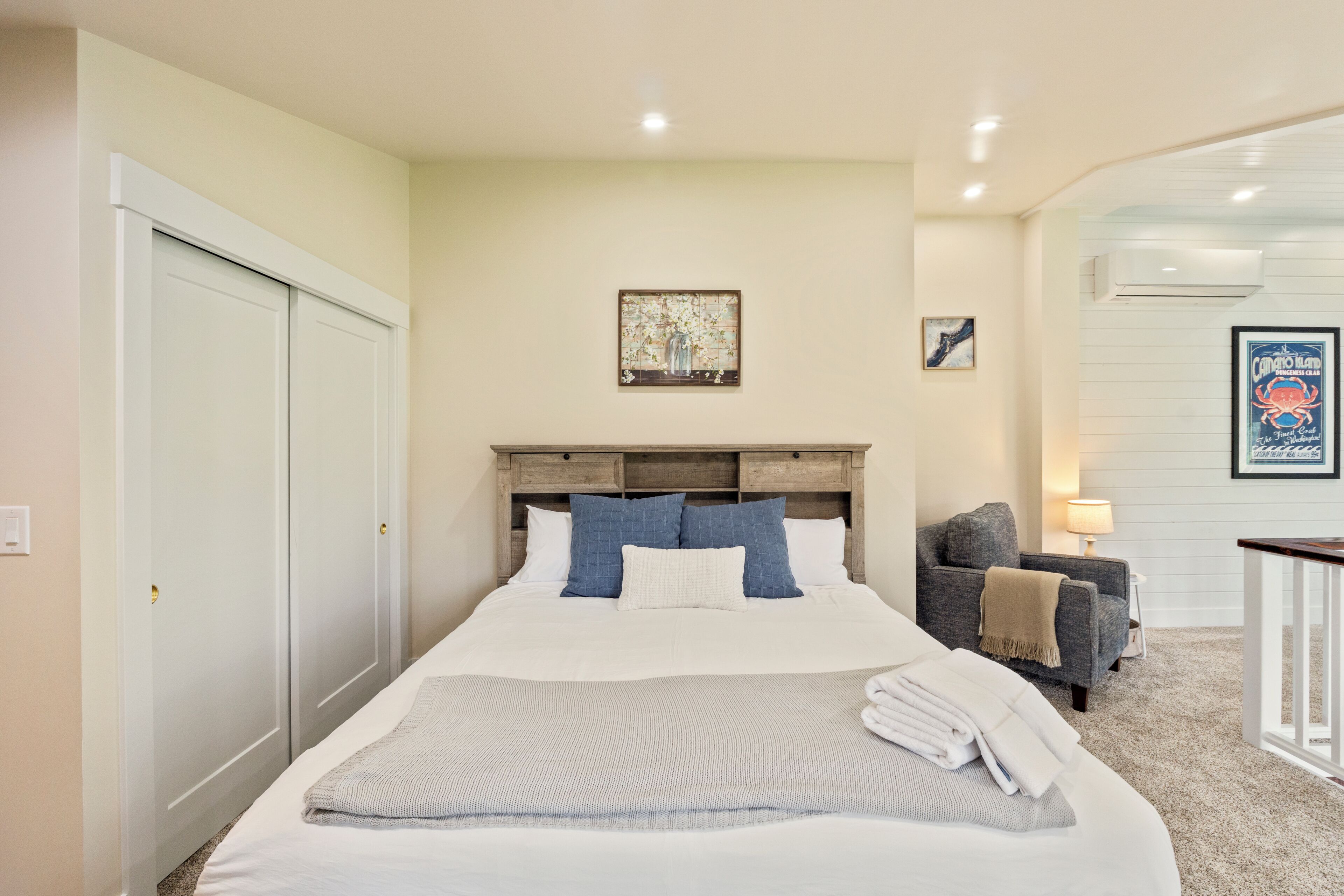 A bedroom with a bed, a headboard, a chair, a lamp, and artwork on the wall.