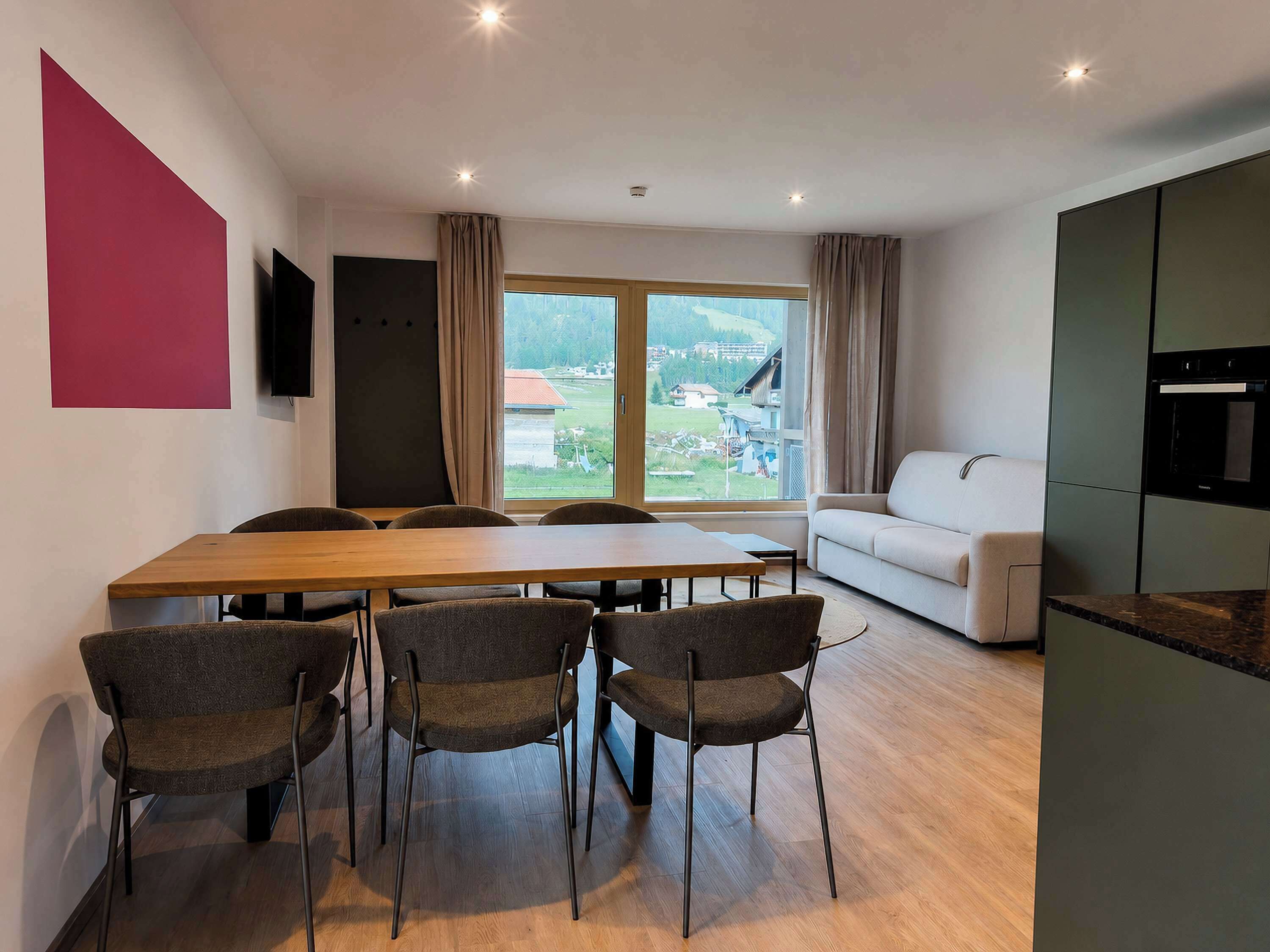 A modern living room with a dining area, a sofa, a TV, and a kitchen area.