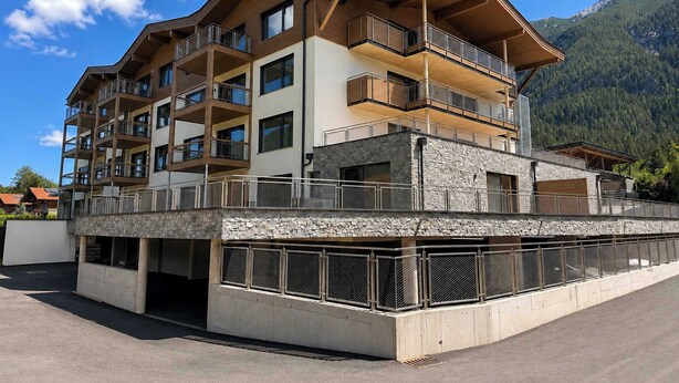 A multi-story hotel with balconies, a stone facade, and a mountainous backdrop. - BASE Achensee Balance N°01 – Garden (Achenkirch)