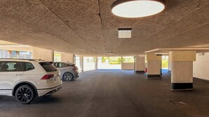 An indoor parking garage with concrete pillars, a white SUV, and a grey sedan. - BASE Achensee Balance N°01 – Garden (Achenkirch)