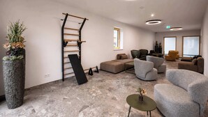 Un'area lounge moderna con pavimento in pietra, divani grigi, una parete da arrampicata in legno e una grande pianta in vaso.