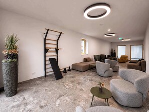 Eine moderne Lounge mit Steinboden, grauen Sofas, einer Holz-Kletterwand und einer großen Topfpflanze.