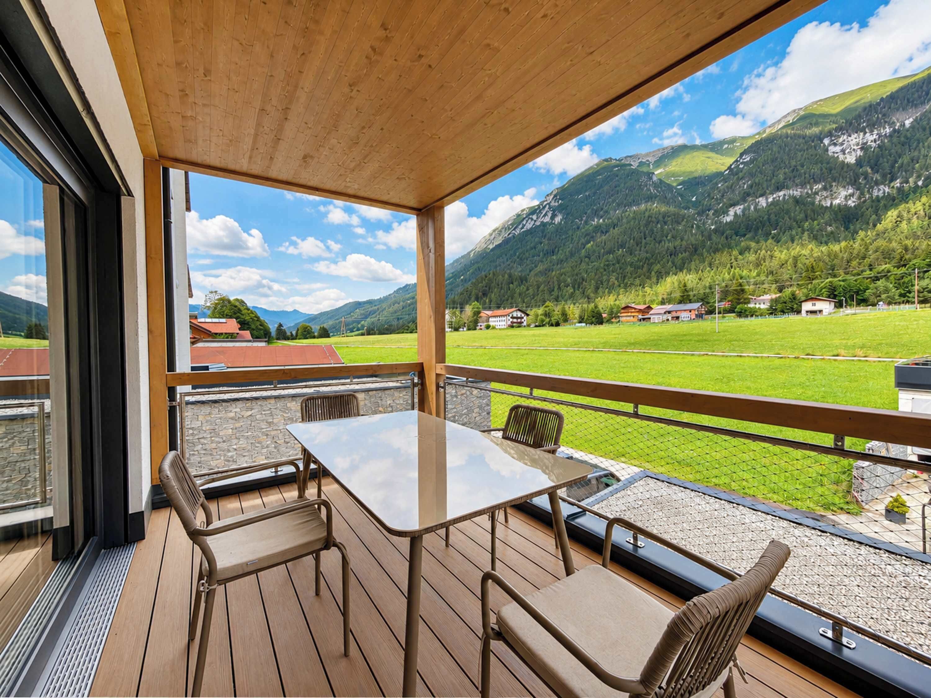 A wooden deck with a table and chairs, overlooking a mountainous landscape with houses in the distance.