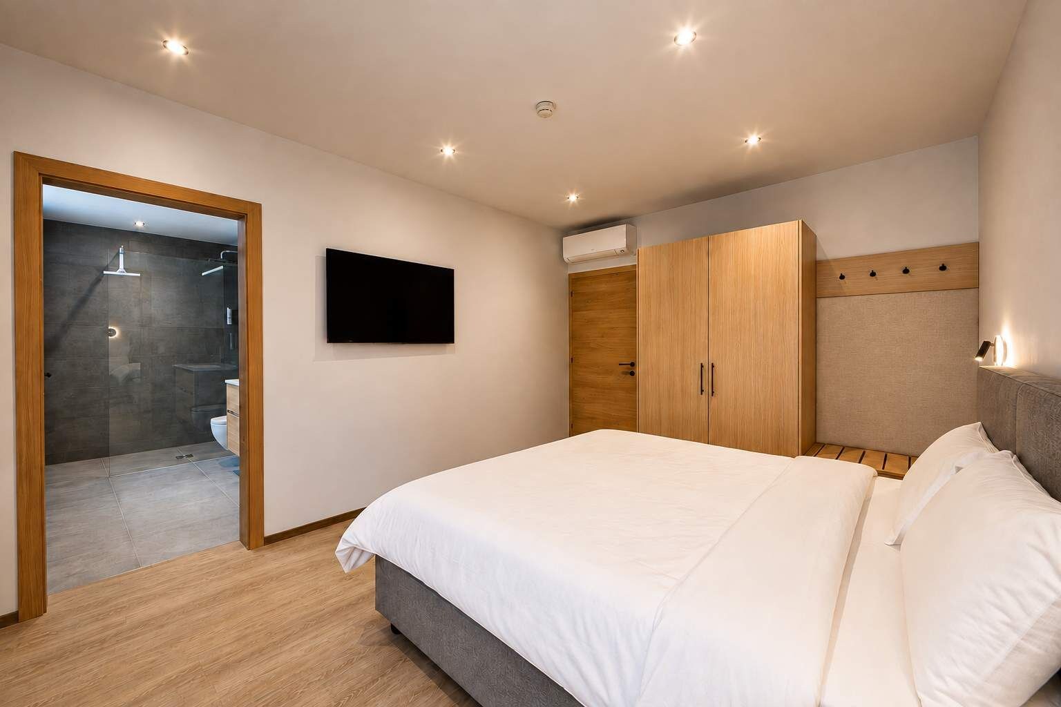 A bedroom with a bed, a wardrobe, a television, and a shower area.