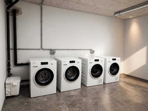 A laundry room with three white front-loading washing machines, a white utility sink, and a grey tiled floor. - BASE Achensee Balance N°05 (Achenkirch)