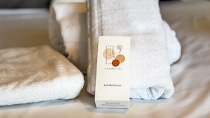 A bathroom kit with a box labeled 'EDEN COSMETICS' on a bed with folded towels. - Studio Terrasse Pointe Croisette A0b214 (Cannes)