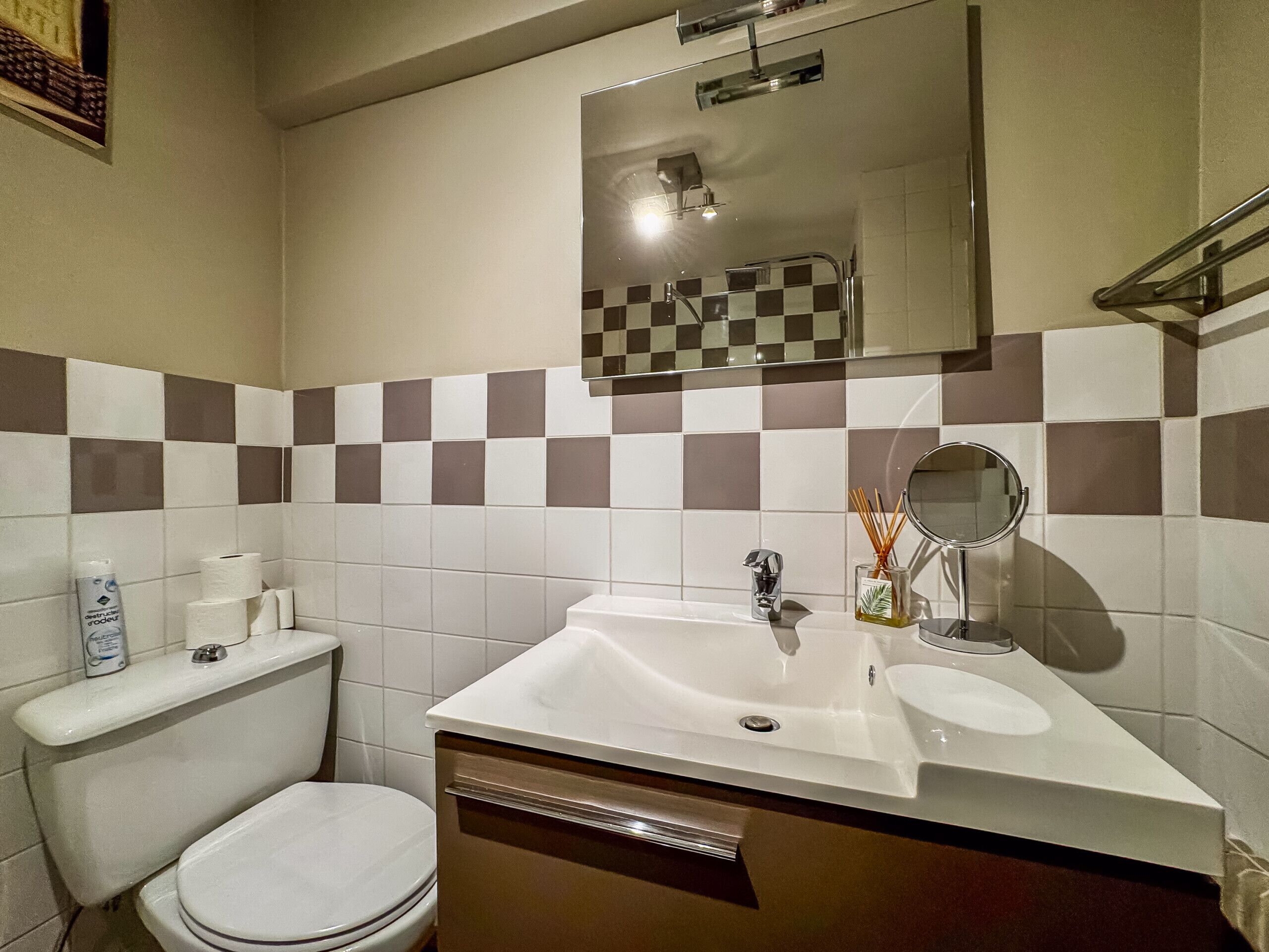 A bathroom with a toilet, sink, mirror, and checkered wall tiles.