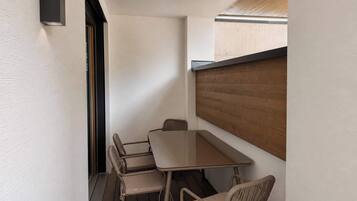 Un pequeño espacio al aire libre con comedor, una mesa y cuatro sillas, un muro de listones de madera y una lámpara en la pared.