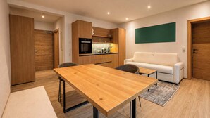 A modern living space with a wooden dining table, a sofa, and a kitchen area. - BASE Achensee Balance N°07 (Achenkirch)