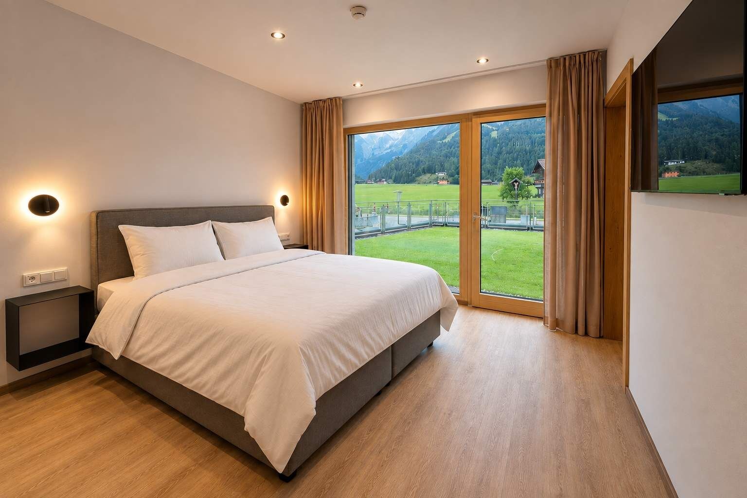 A modern bedroom with a large bed, a nightstand, a wall-mounted light, and a sliding glass door leading to a balcony with a view of a green landscape and mountains.