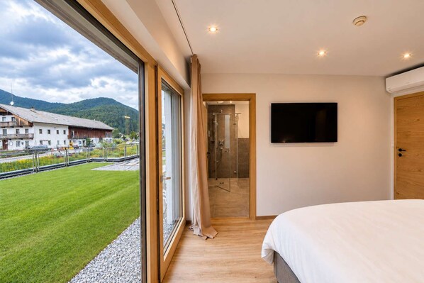 Ein Schlafzimmer mit großem Fenster, einem Bett, einer Dusche und einem Fernseher.