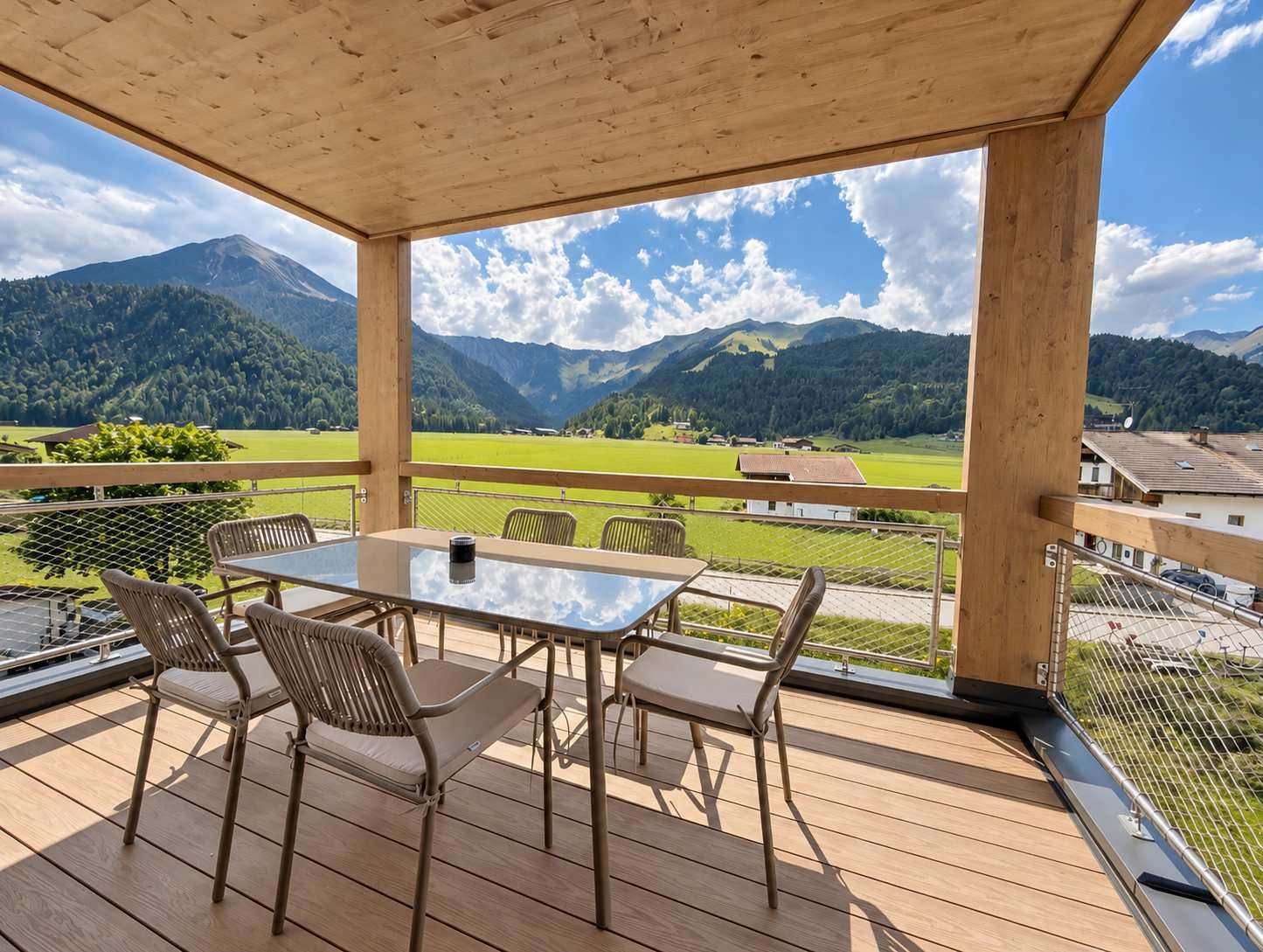A wooden deck with a glass table and chairs, overlooking a mountainous landscape.