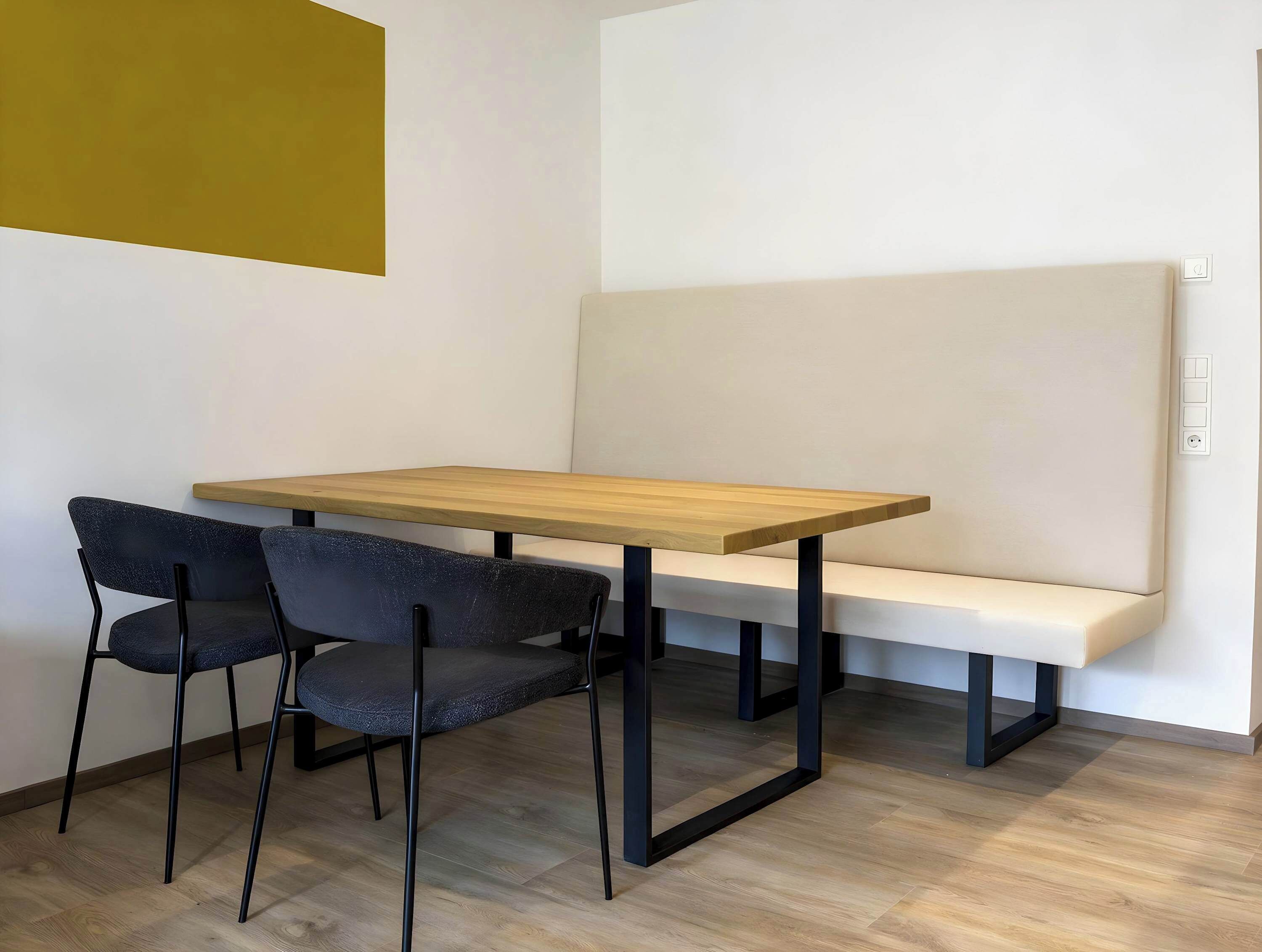 Una habitación con una mesa de madera, dos sillas, un banco y una pared de color claro.