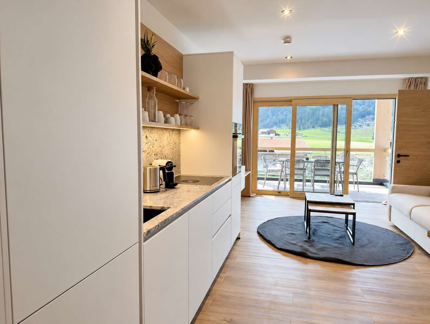 Eine moderne Küche mit einem großen Fenster, einem Essbereich mit einem runden Teppich und Blick ins Freie.