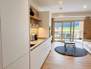 Eine moderne Küche mit einem großen Fenster, einem Essbereich mit einem runden Teppich und Blick ins Freie.
