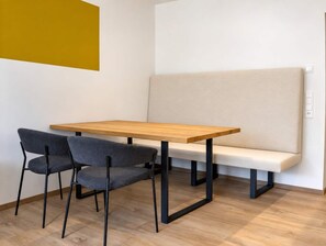 Ein schlichter Raum mit einem Holztisch, zwei Stühlen, einer Bank und einer gelben Wand.