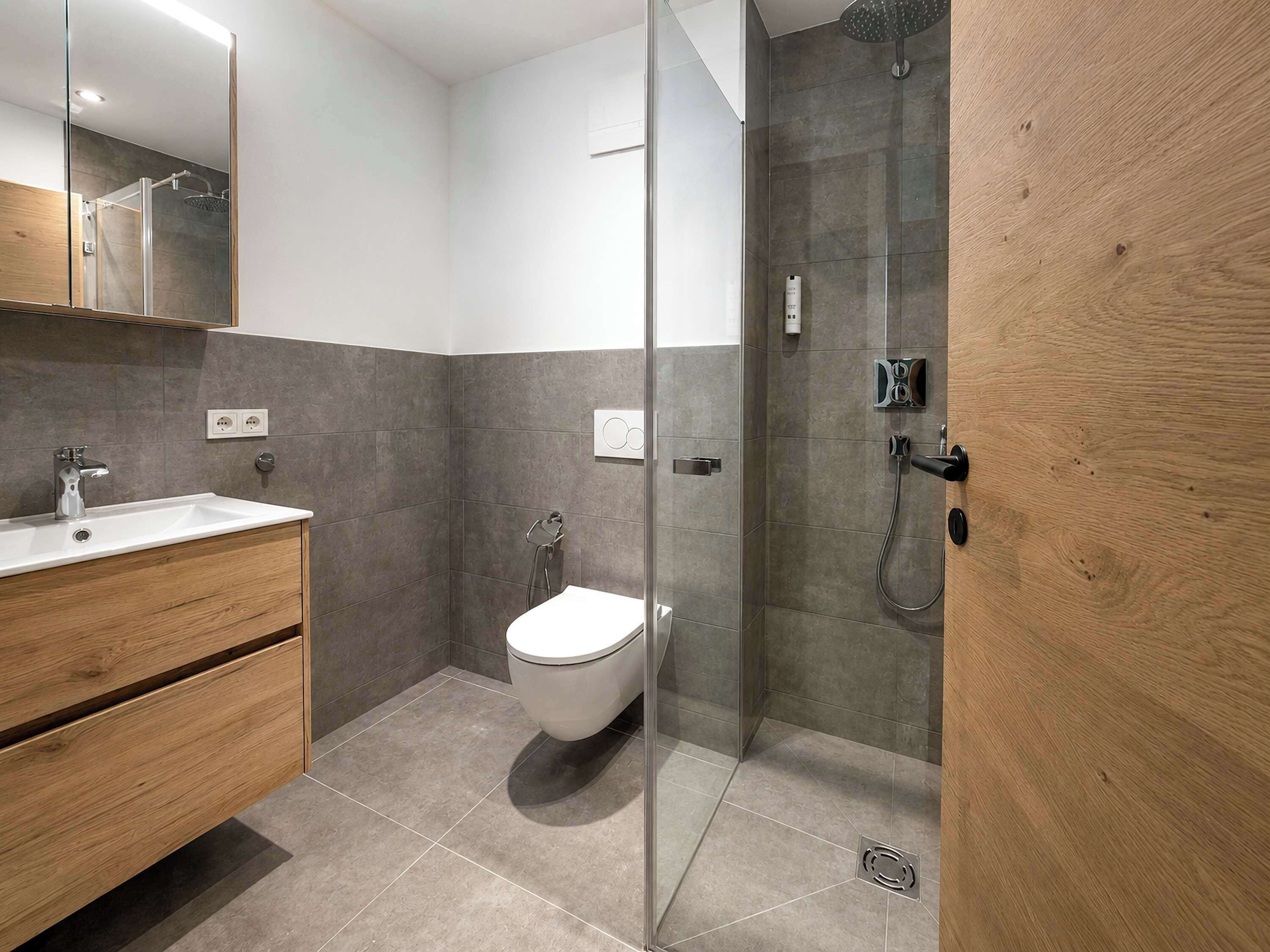 Een moderne badkamer met een douchecabine van glas, een wit toilet en een houten wastafelmeubel.