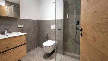 Een moderne badkamer met een douchecabine van glas, een wit toilet en een houten wastafelmeubel.