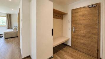 Ein modernes Zimmer mit Holztür, weißem Kleiderschrank, einer Bank und einem Fenster mit Vorhängen.