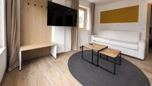 A modern living room with a flat-screen TV mounted on a wooden wall, a white sofa, a small wooden coffee table, and a grey rug. - BASE Achensee Energy N°21 (Achenkirch)
