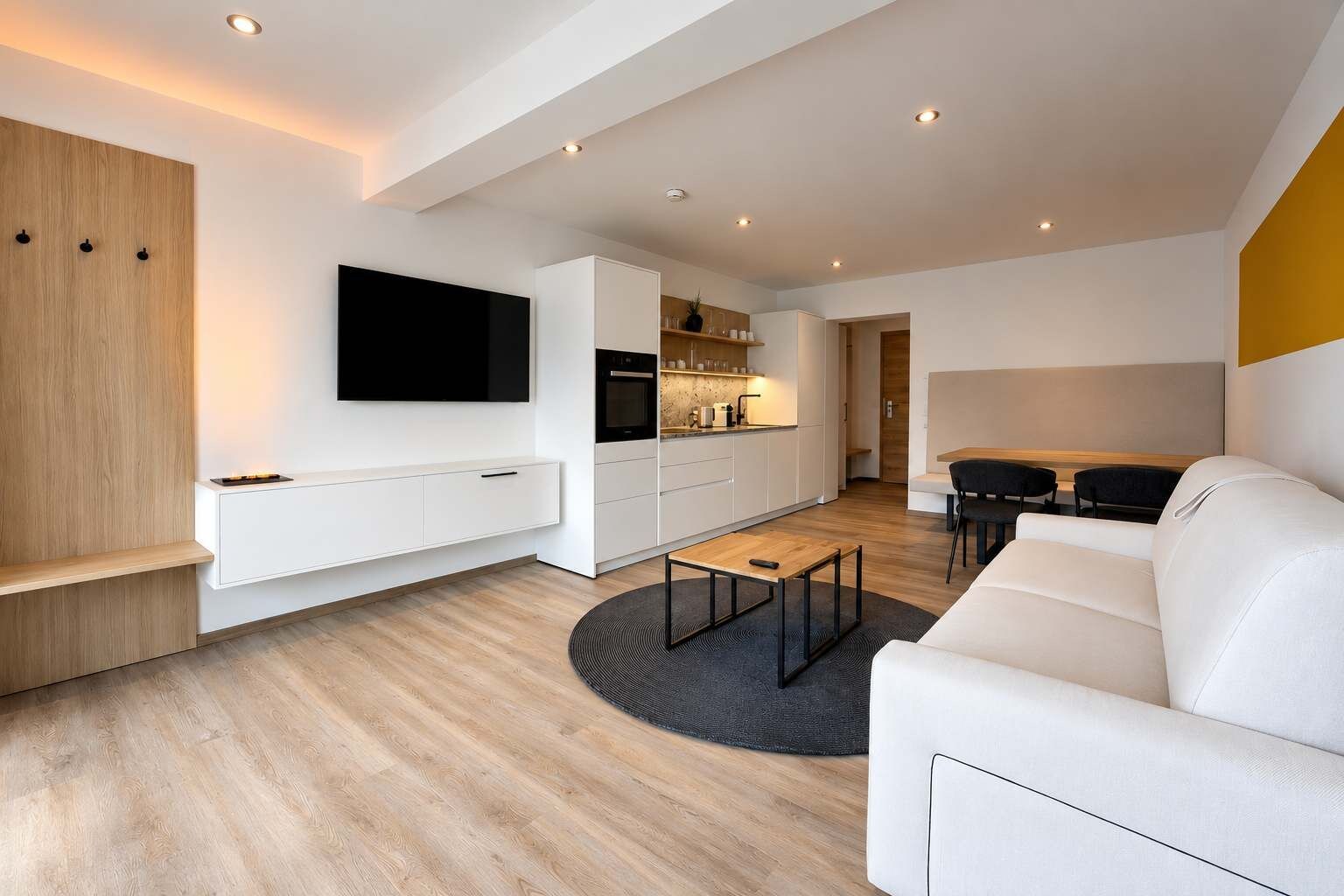 A modern living room with a flat-screen TV, a dining area, and a kitchen.