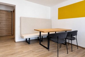 Ein Zimmer mit einem Holztisch, zwei Stühlen, einer Bank und einer gelben Akzentwand.
