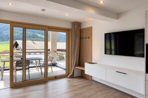 Et moderne interiør med en skydedør til en balkon, et vægmonteret fladskærms-tv og en minimalistisk træbænk.