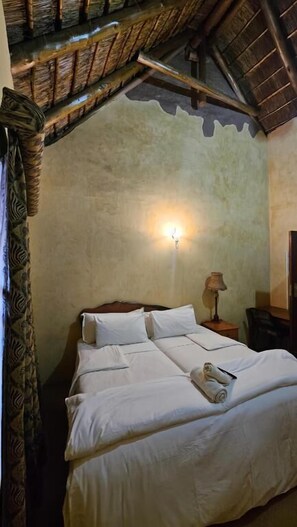 Una cama con ropa blanca, una mesita de noche con lámpara y un aplique de pared.