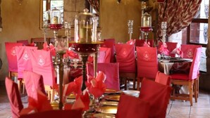 A dining area with tables set for service, chairs covered with red tablecloths, and a chandelier.