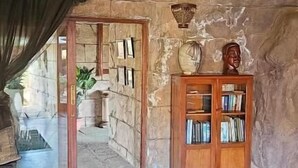 A stone-walled room with a wooden ceiling, a bookshelf, and a doorway leading to an outdoor area.