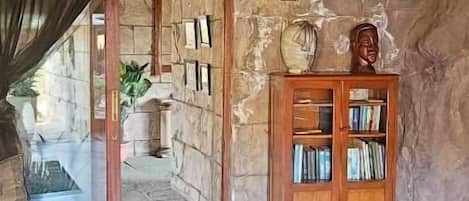 Una habitación con paredes de piedra, techo de madera, una estantería y un acceso a un espacio exterior.