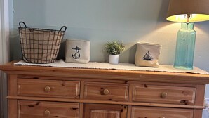 Een houten dressoir met meerdere lades, een geweven mand, een kleine potplant en een lamp.